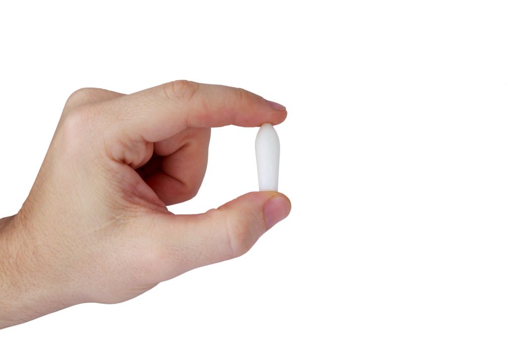 A hand holding a small vitamin e vaginal suppository to demonstrate its size.